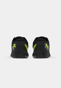 Zapatillas deportivas negras con una superficie texturizada, que cuentan con un logotipo y acentos en verde brillante, un diseño de perfil bajo y una suela duradera.