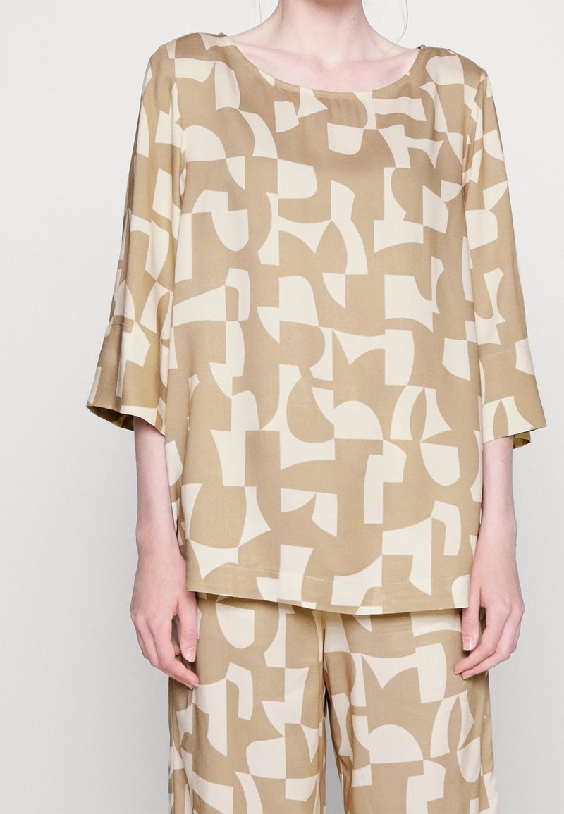 Tunique beige avec motifs géométriques crème, dotée d'un col rond et de manches amples, confectionnée dans un tissu lisse et léger.