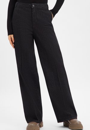 Schwarze Jeans mit weitem Bein und hoher Taille, versehen mit dezenten vertikalen Linien und Vorderseiten-Taschen. Metallischer Knopfverschluss an der Taille.