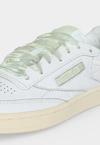 Λευκό αθλητικό παπούτσι Reebok με διαφανή κορδόνια από σατέν, υφή στη σόλα και μαλακό επένδυση στον γιακά.