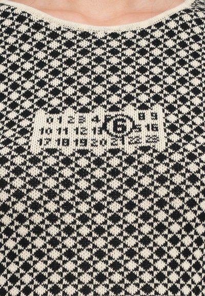 Svart och krämfärgad mönstrad stickad tröja med geometriskt mönster och en broderad logodetalj i mitten. Rund halsringning, texturerad tyg.
