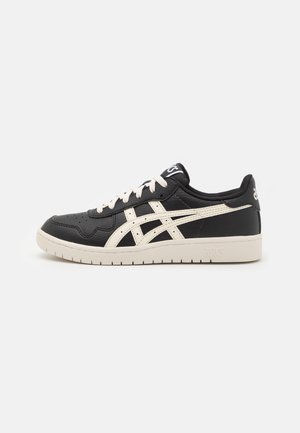 Baskets basses ASICS en noir et blanc avec lacets blancs, bandes caractéristiques et semelle claire sur un fond uni.