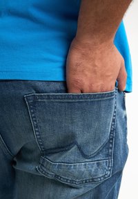 Jeans z denimu w wyblakłym niebieskim kolorze, z tylną kieszenią przeszytą charakterystycznym zakrzywionym wzorem. Ręcznie umieszczone w kieszeni.