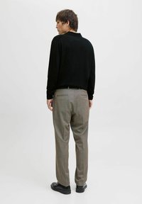 Juodas ilgas rankovėmis polo marškinėliai derinami su šviesiai pilkomis kelnėmis, turinčiomis tiesų kirpimą ir subtilų languotą raštą, baigiama juodais batais.