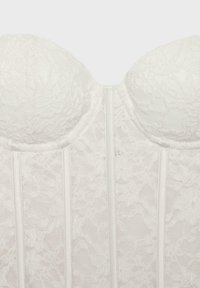 Bustier en dentelle blanche avec bonnets structurés et armatures verticales.