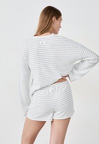 Szary i biały zestaw odzieży domowej w paski z krótkim topem z długim rękawem i pasującymi szortami, wykonany z miękkiego materiału z prostymi metkami z tyłu.