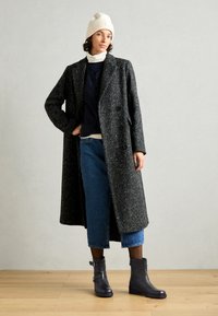 Long black and white speckled coat with double buttons, paired with a navy top and denim cropped pants. Finished with black ankle boots.