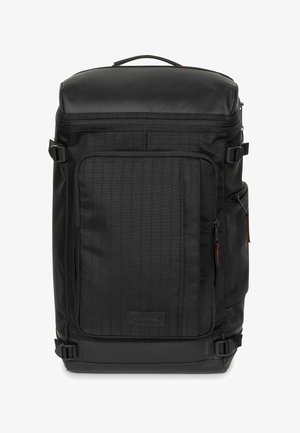 Mochila negra con un exterior de tela texturizada, cierre superior con cremallera, bolsillo frontal y correas laterales. Presenta un parche con el logo y herrajes duraderos.