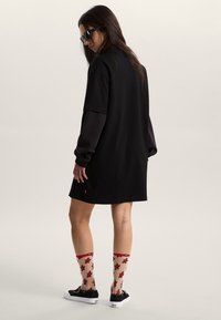 Robe t-shirt noire oversize, manches courtes, tissu lisse. Motif d'étoiles rouges et noires sur des chaussettes transparentes montant jusqu'aux genoux. Chaussures noires à lacets.
