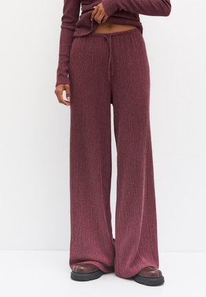 Personne portant un pantalon en maille côtelée taille haute à jambes larges et un haut à manches longues assorti de couleur mauve foncé, debout sur un fond blanc.