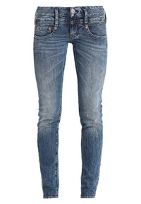 Tight jeans i medelblå denim. Har en knapp- och dragkedjeslutning, fem fickor och subtila slitningar längs låren.