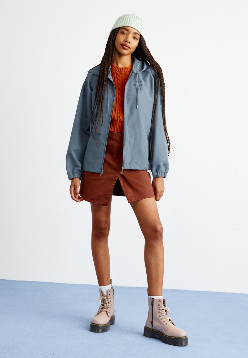 Blau leichte Jacke mit Kapuze, orangefarbener Grobstrickpullover, braut Denimrock und beige Stiefel mit schwarzen Sohlen und Reißverschlüssen.