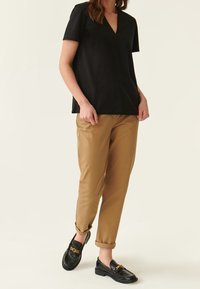 Sort kortærmet V-hals top parret med tan bukser med opfoldede manchetter og sorte loafers med en guld kæde accent.