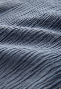 Mjuk blå tyg med jämnt fördelade vertikala räfflor och subtila veck som skapar en texturerad, vågig yta.