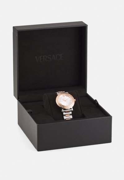 Versace óra fekete dobozban. Kerek rózsa arany tok, fehér számlap görög kulcs mintázattal, valamint ezüst és arany fém karkötő.