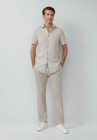 Kurzärmeliges, hellbeiges Button-Down-Hemd mit strukturiertem Muster, kombiniert mit hellgrauen Hosen und weißen Sneakers.