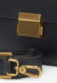 Czarna skórzana torba z żłobionym złotym zapięciem i dopasowanym odczepianym paskiem z złotym obrotowym hakiem i zapięciem.