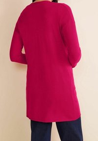 Svetr s dlouhým rukávem v barvě fuchsie, s kulatým výstřihem a volným střihem, zobrazený zezadu na světlém pozadí.