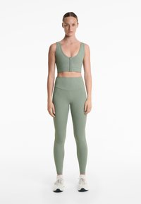Grön ribbad crop top med knappar och matchande högmidjade leggings, med en mjuk textur och figurnära silhuett, tillsammans med vita sneakers.