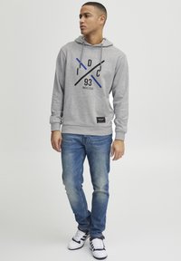 Gray hoodie with a drawstring, featuring a graphic design in black and blue, paired with blue jeans and white sneakers.