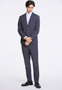 Marinblått pinstripe-kostym med en enknappad blazer och matchande byxor, kombinerat med en vit skjorta och svarta lackskor.