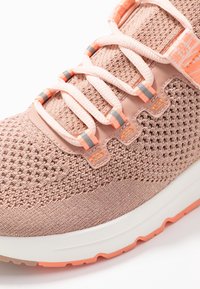 Ljust rosa träningsskor med en vävd mesh-överkonstruktion, elastiska snörningar och en texturerad sula med orange detaljer och en vit mellansula.