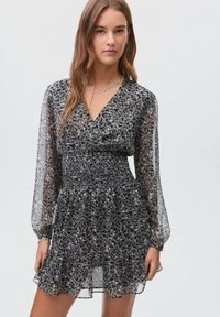 Černobíle vzorované šaty s výstřihem do V, nařaseným pasem, dlouhými průhlednými rukávy a volánovým lemem. Vyrobeno z lehkého, splývavého materiálu.