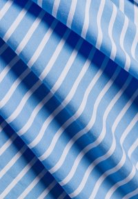 Tessuto blu con righe bianche ondulate; texture liscia; le pieghe creano profondità e ombre, enfatizzando il motivo e il contrasto dei colori.