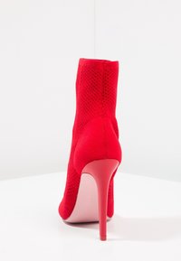 Bottine à talon aiguille rouge avec un dessus texturé et des détails en mesh. Présente un bout pointu et un talon stiletto. Doublure intérieure lisse.