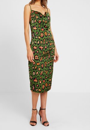 Mujer con un vestido midi de tirantes verde con estampado de leopardo multicolor y sandalias negras de tacón alto con tiras al tobillo, posando frente a un fondo sencillo.