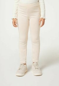 Jasnobeżowe legginsy z elastycznego materiału, o dopasowanym kroju i elastycznym pasie. W połączeniu z jasnymi trampkami.