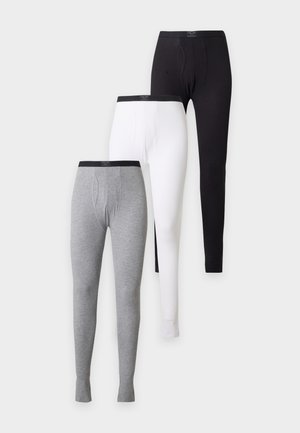 Homme torse nu, debout pieds nus, portant des leggings longs noirs moulants sur un fond clair uni.
