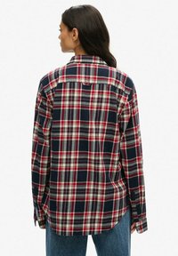 Camicia in flanella a quadri nei colori blu navy, rosso e grigio. Presenta un colletto a punta e polsini con bottoni. Tessuto di cotone con una vestibilità morbida.