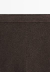 Gros plan sur un tissu tricoté marron foncé avec une couture verticale visible et une large section de ceinture horizontale.