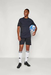 Urheiluasusetti sisältää mustan lyhythihaisen paidan ja mustat shortsit. Lisävarusteet: valko-mustaraidalliset sukat, mustat kengät ja värikäs jalkapallo.