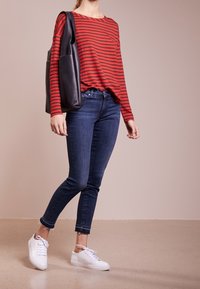 Röd och svart randig långärmad topp, blå slim fit jeans med fransar i nederkant, och vita sneakers. Svart axelväska med fickor.