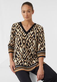 V-Ausschnitt-Oberteil mit einem schwarzem, cremefarbenem und orangefarbenem Ikat-Muster. Dreiviertelärmel mit einem kontrastierenden schwarzen und orangefarbenen Band am Saum.