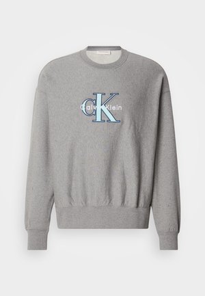 Szara bluza z okrągłym dekoltem, z prążkowanymi mankietami i dołem, z niebiesko-białym logo "Calvin Klein" na środku. Klasyczny krój.