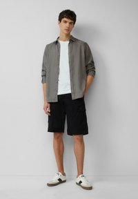 Lichtgrijs overhemd met knopen, wit T-shirt, zwarte cargoshorts en witte sneakers met grijze accenten. Eenvoudig ontwerp en casual pasvorm.