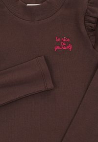 Bruine geribde lange mouwen top met een ronde hals, voorzien van gerimpelde accenten op één schouder en roze geborduurde tekst: "wees lief voor jezelf."