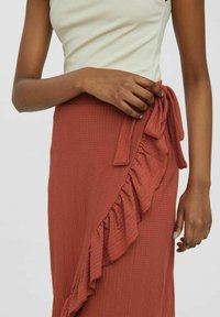 Miedziano-ruda spódnica midi z teksturowanej tkaniny, z falbaniastym detalem po boku i zawiązywanym paskiem w talii. Gładki, dopasowany fason.