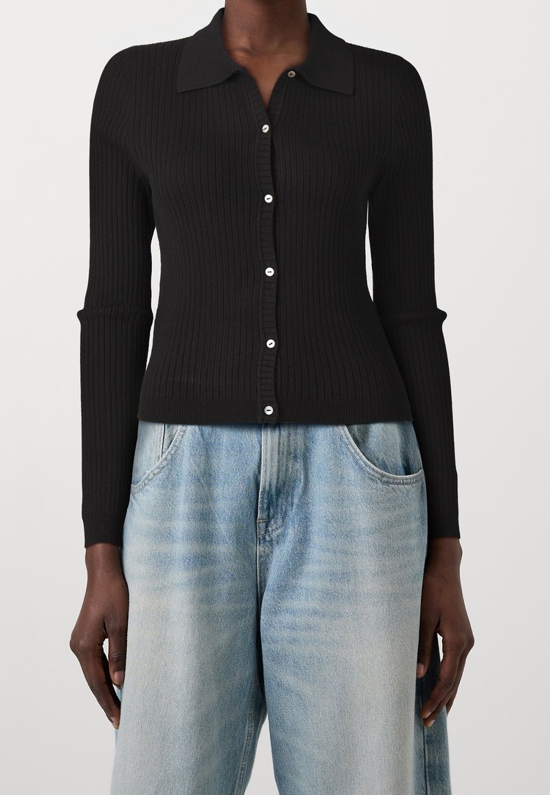 Personne portant un cardigan noir côtelé boutonné à manches longues associé à un jean taille haute bleu clair.