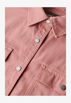 Light pink shirt featuring a textured fabric, pointed collar, and silver snap buttons with "Superdry" embossed logo. Two chest pockets.