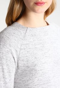 Grå, texturerad tröja med rundad halsringning och raglanärmar. Materialet verkar mjukt och har ett subtilt, varierat mönster.