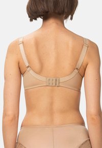 Kvinde set fra ryggen iført en beige bh med justerbare stropper og hægtsystem bagpå, parret med matchende trusser.