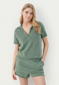 Grønt frotté to-dels sæt bestående af en skjortekrave kortærmet top og shorts med elastisk talje, med en blød, tekstureret finish.