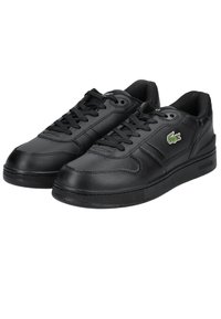 Paire de baskets en cuir noir avec lacets noirs et logo crocodile vert sur le côté extérieur, design bas et semelles en caoutchouc texturées.