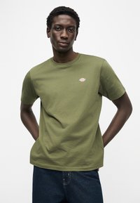 Χακί βαμβακερό t-shirt με στρογγυλή λαιμόκοψη και κοντά μανίκια. Περιλαμβάνει μικρή λεπτομέρεια λογότυπου στο στήθος. Άνετη εφαρμογή.