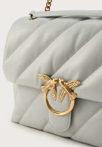 Γκρι δερμάτινη τσάντα ώμου με διαγώνιο σχέδιο με ραφές, χρυσό μεταλλικό διακοσμητικό σε σχήμα πουλιού και αλυσίδα ως λουρί.