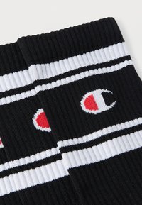 Chaussettes en coton noir avec des rayures blanches et noires, arborant un logo rouge et blanc bien visible. Texture côtelée au niveau du bord pour un ajustement confortable.